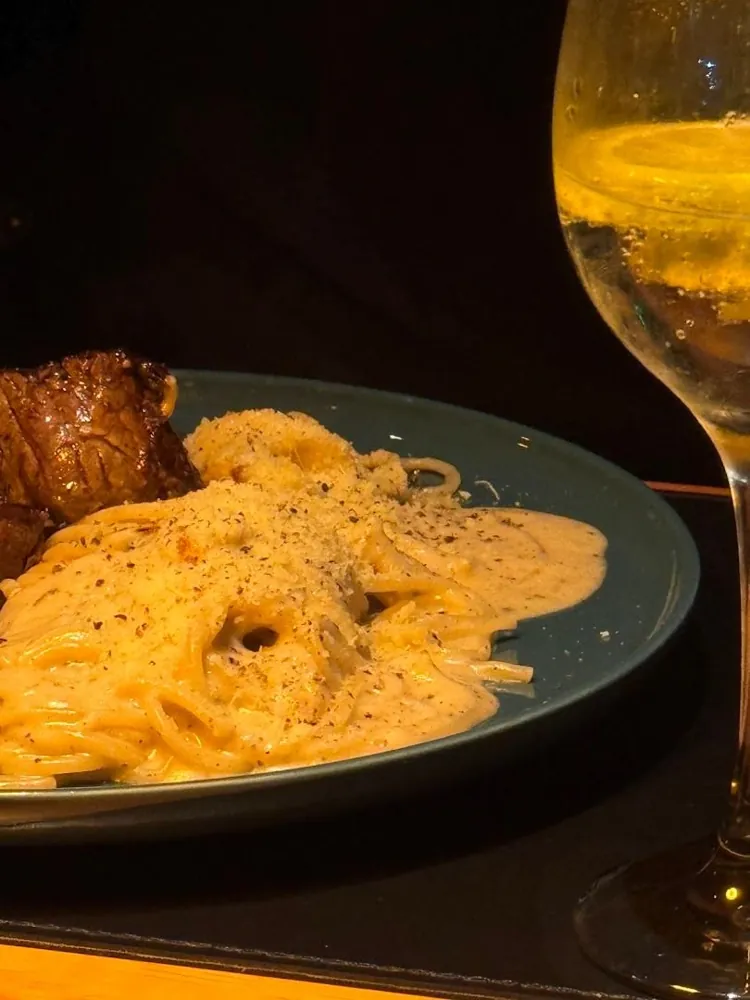 Prato de massa com carne e taça de vinho na mesa do Di. Pippo